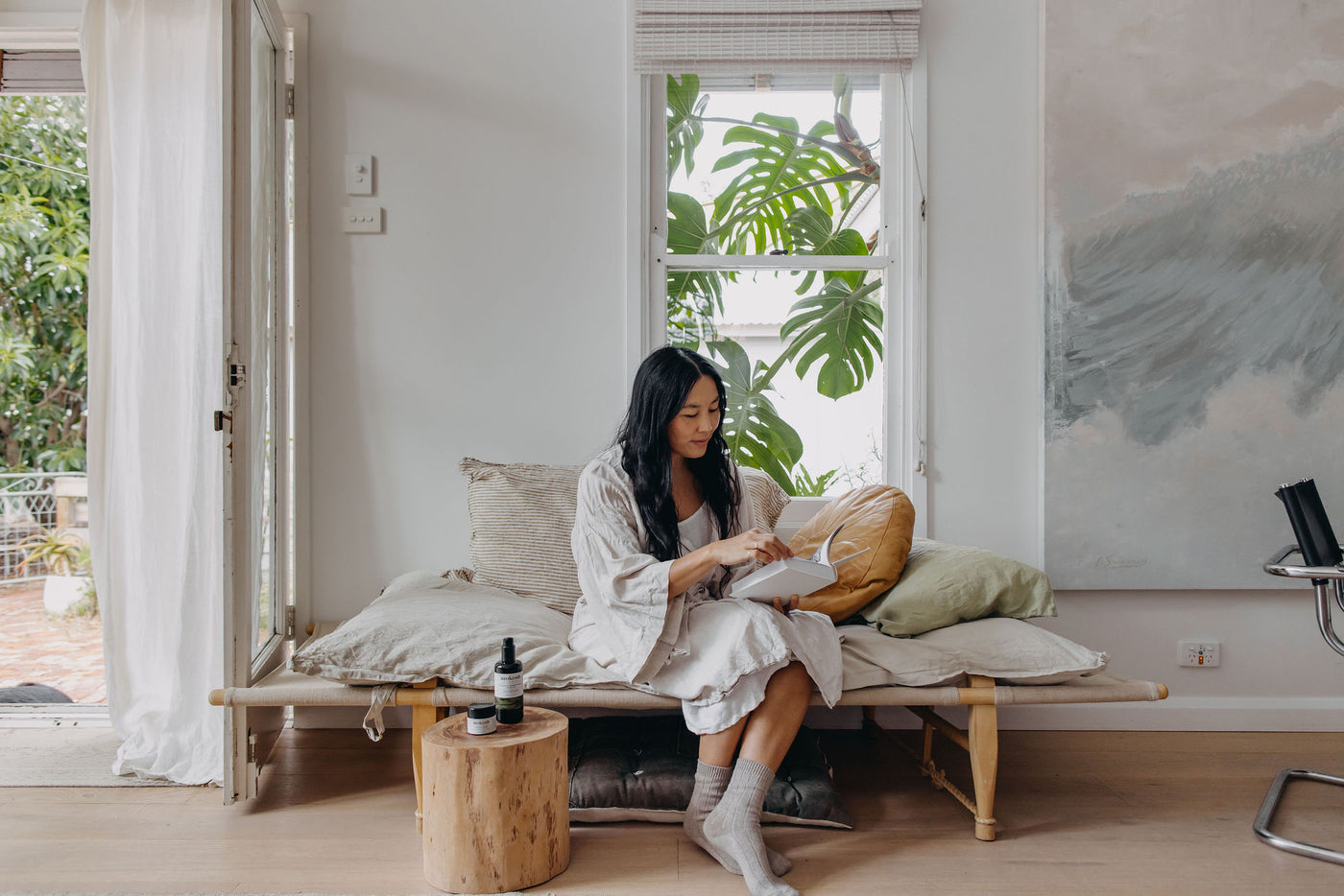Woman sitting on a wooden bench in a bright room with large windows and plants.