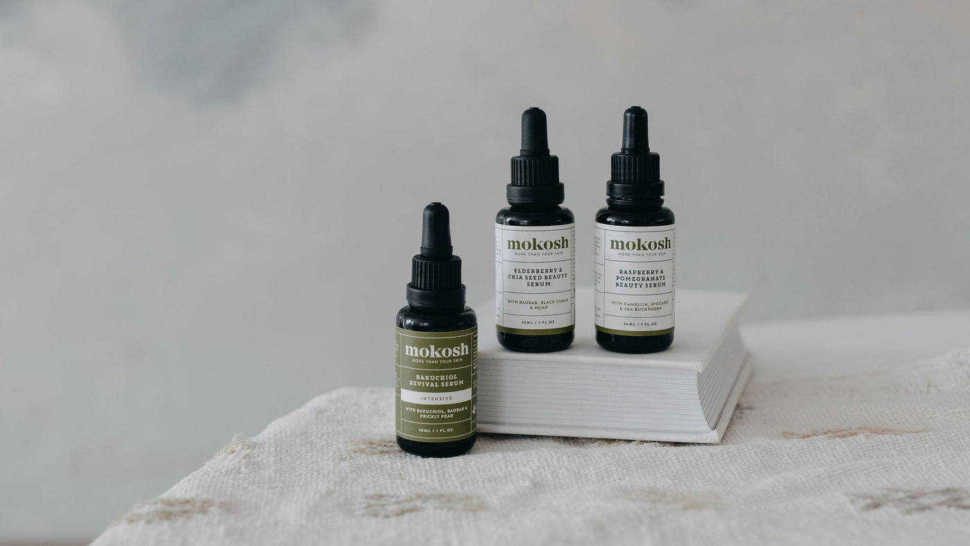 Three mokosh skincare bottles on a white surface with a gray background